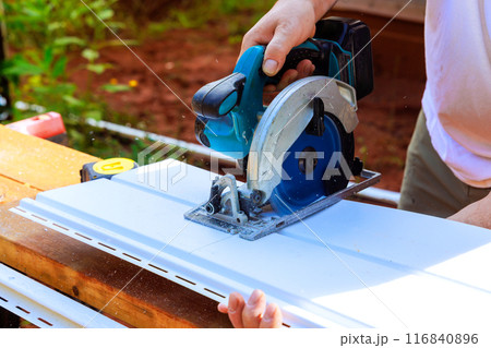 Using circular handsaw, worker cuts plastic vinyl siding to size prior to installation 116840896