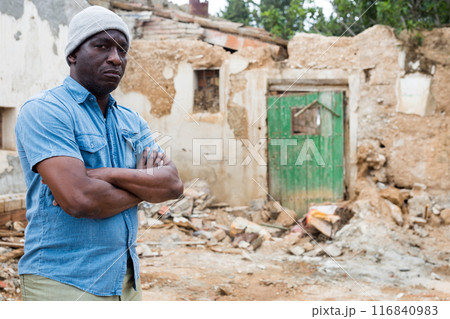 Man is standing beside destroyed house 116840983