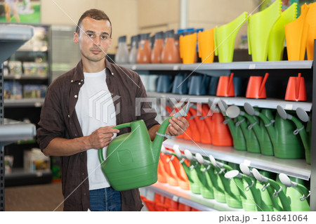 Amateur gardener guy selects watering can for hobby in greenhouse flower-bed 116841064