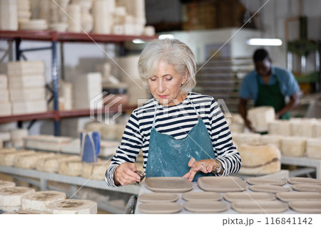 Mature woman processing new clay plates in workshop 116841142