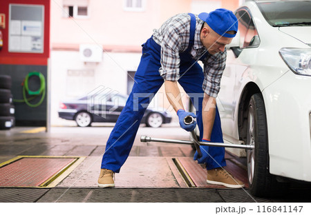 Mechanic engaged in replacement of tyre on car wheel in workshop Mechanic engaged in replacement of tyre on car wheel in workshop 116841147