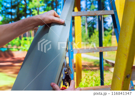 Using scissors, worker cuts plastic vinyl siding to size prior to installation Using scissors, worker cuts plastic vinyl siding to size prior to installation 116841347