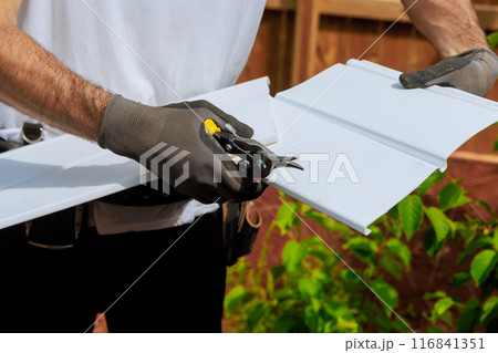 An individual cuts plastic vinyl siding to size before it is installed using scissors An individual cuts plastic vinyl siding to size before it is installed using scissors 116841351