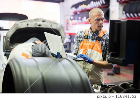 Male mechanic using laptop while repairing car in service Male mechanic using laptop while repairing car in service 116841352