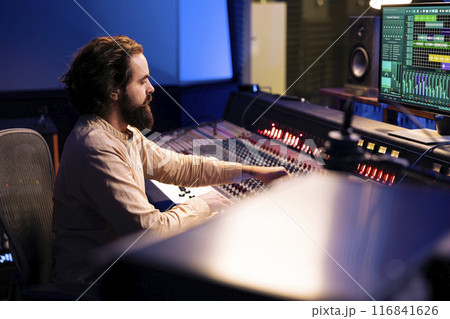 Control room audio engineer processing and mixing sounds with sliders and knobs, working on music post production in professional studio. Technician producing tracks on electronic console. 116841626