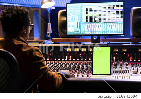 Audio engineer editing music on control desk panel board, recording tracks to add sound effects in post production. Technician producer looks at device with mockup layout in studio. Audio engineer editing music on control desk panel board, recording tracks to add sound effects in post production. Technician producer looks at device with mockup layout in studio. 116841694