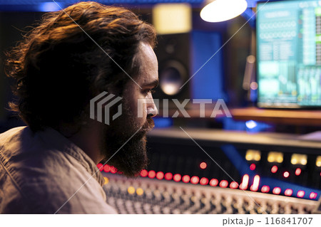 Sound designer working on producing a new album in professional studio, mixing and mastering tracks in control room. Audio technician editing audio recordings using sliders and faders on board. Sound designer working on producing a new album in professional studio, mixing and mastering tracks in control room. Audio technician editing audio recordings using sliders and faders on board. 116841707