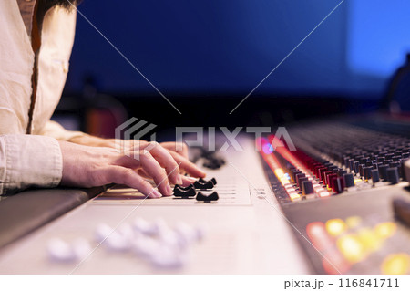 Music producer pushing faders and sliders on control panel board in studio, adjusting volume levels on songs and removing white noise. Sound engineer operates technical equipment. Close up. Music producer pushing faders and sliders on control panel board in studio, adjusting volume levels on songs and removing white noise. Sound engineer operates technical equipment. Close up. 116841711