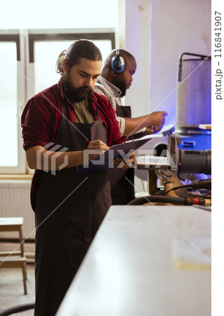 Craftsperson looking over technical drawings of commission on notepad to make creative wood art. Manufacturer looking at blueprints to execute furniture assembling woodworking project 116841907