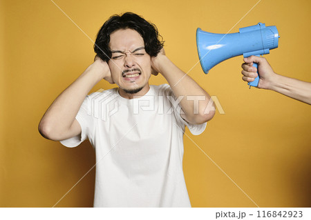 カラーバックで拡声器の音で耳を塞ぐ男性 116842923