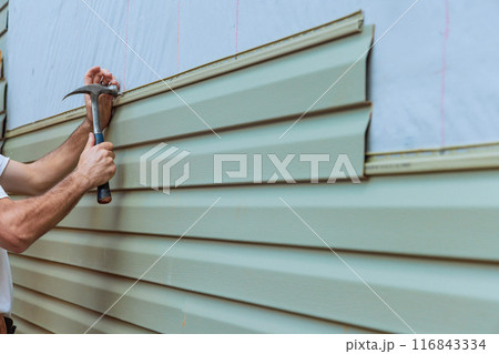 Contractor installing vinyl siding plastic panels on facade wall of new home 116843334