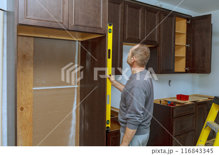 Installation of new kitchen cabinets requires worker to hang level in order to ensure that cabinets are level 116843345