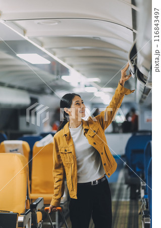 Young Female Tourist with Luggage Walking Through Airplane Cabin Ready for Travel Adventure 116843497