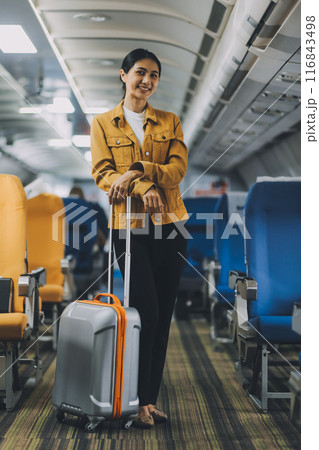 Young Female Tourist with Luggage Walking Through Airplane Cabin Ready for Travel Adventure Young Female Tourist with Luggage Walking Through Airplane Cabin Ready for Travel Adventure 116843498