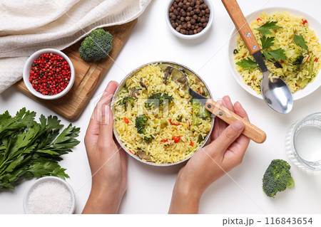 Pilaf, spices, spoons and hands on white background, top view 116843654