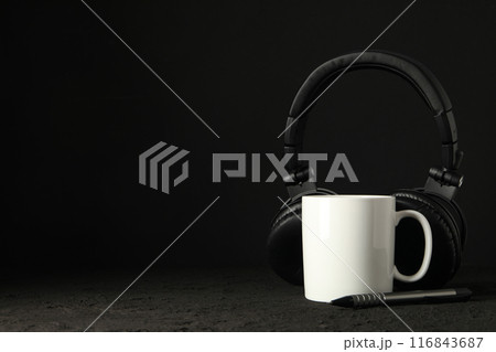 White cup with black headphones on a dark background 116843687