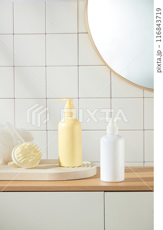 Photograph of bathroom concept was taken from frontal on white checkered brick wall background. Two bottle of shower gel or shampoo without label displayed on top of wooden cabinet Photograph of bathroom concept was taken from frontal on white checkered brick wall background. Two bottle of shower gel or shampoo without label displayed on top of wooden cabinet 116843719