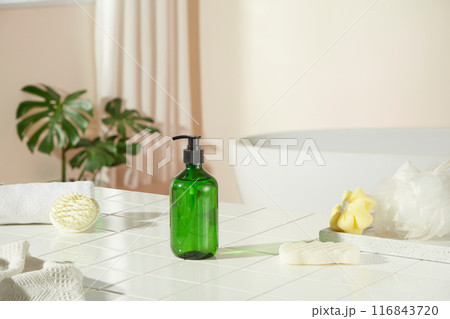 Frontal shot at a unbranded green shampoo bottle, which displayed on a brick bathroom floor, surrounded by some items for bathing. Blank space for advertising or adding text Frontal shot at a unbranded green shampoo bottle, which displayed on a brick bathroom floor, surrounded by some items for bathing. Blank space for advertising or adding text 116843720