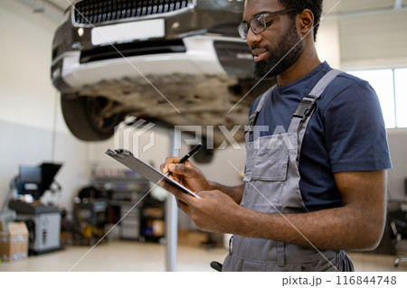 Mechanic inspecting car in auto repair shop with clipboard Mechanic inspecting car in auto repair shop with clipboard 116844748