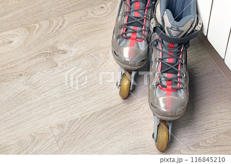 Old roller skates with cloth shoe and plastic base near radiator on wood floor with rubber wheels. Sports and equipment.  116845210