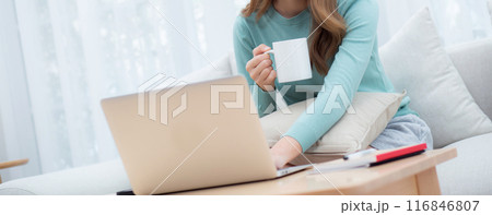 Young asian woman wearing glasses sitting sofa working on laptop computer and drinking coffee. Young asian woman wearing glasses sitting sofa working on laptop computer and drinking coffee. 116846807