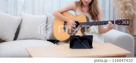 Young asian woman sitting on sofa looking tablet for practice music with guitar in living room. Young asian woman sitting on sofa looking tablet for practice music with guitar in living room. 116847410