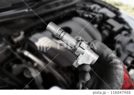 A mechanic hand holds an ignition coil for a spark plug of a car engine A mechanic hand holds an ignition coil for a spark plug of a car engine 116847488