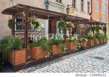 Summer street in the old town of Riga, Latvia. Wooden boxes with beautiful flowers outside a cafe. Summer street in the old town of Riga, Latvia. Wooden boxes with beautiful flowers outside a cafe. 116848121