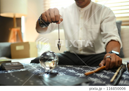 Mysterious fortune teller holding an iron pendulum forecasting over crystal ball. Divination concept Mysterious fortune teller holding an iron pendulum forecasting over crystal ball. Divination concept 116850006