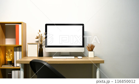 Minimalist home office, computer monitor with blank screen and wooden bookshelf near white wall Minimalist home office, computer monitor with blank screen and wooden bookshelf near white wall 116850012