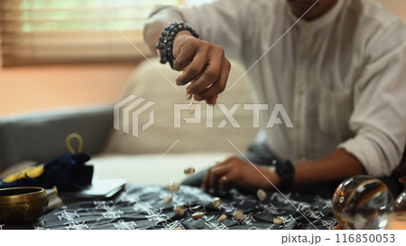 Shot of mysterious fortune teller scattering shells on a table with a mystical cloth. Divination concept Shot of mysterious fortune teller scattering shells on a table with a mystical cloth. Divination concept 116850053