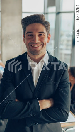 Portrait of smiling businessman with crossed hands standing in office on colleagues background 116850264