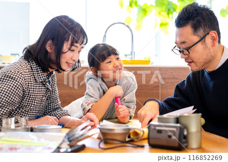 家族で防災用品を並べて防災会議をお父さんが主導で行っている様子を笑顔で見つめる娘 家族で防災用品を並べて防災会議をお父さんが主導で行っている様子を笑顔で見つめる娘 116852269