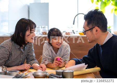 家族みんなで防災に関するお話をお父さん主導で行っている様子を楽しそうに見つめる娘とお母さん 116852271