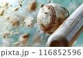 A dynamic image showing a baseball mid-air, seemingly thrown from a leather glove, with a bat poised to hit. The ball's stitches and slight dirt marks are in sharp focus, while the glove's leather 116852596