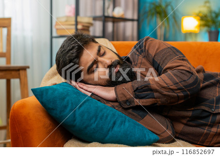 Tired Indian young man lying down in bed taking a rest at home, napping, falling asleep on sofa 116852697