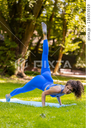 Caucasian young woman in yoga Cobra pose stretches upward morning fitness routine on mat in park 116853019