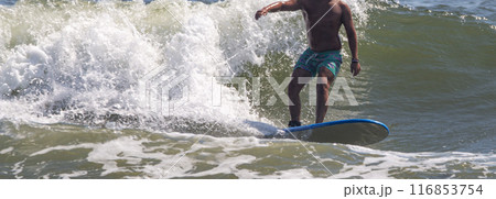 Man surfing with a wall of water of a breaking wave behind him Man surfing with a wall of water of a breaking wave behind him 116853754