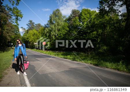 The teenager returns on foot along the asphalt road among lush greenery - wonderful trees and shrubs. 116861349