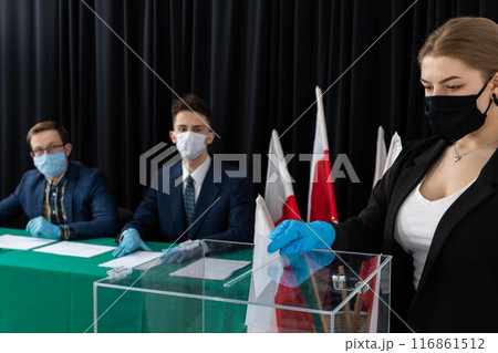 A teenager throws a completed electoral card into the transparent ballot box. 116861512
