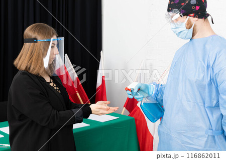 A woman from an election commission disinfects her hands before sitting at an election table. A woman from an election commission disinfects her hands before sitting at an election table. 116862011