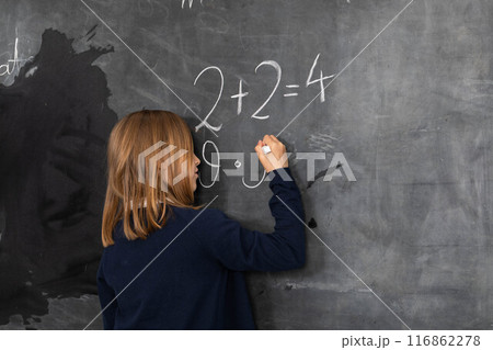 The student solves a math problem standing at the blackboard in her classroom. The student solves a math problem standing at the blackboard in her classroom. 116862278