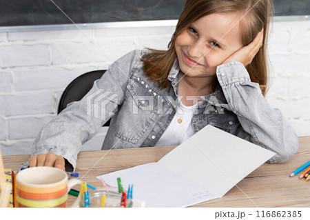 The schoolgirl sits at a school bench and supports her head with her hands in anticipation of a teacher. The schoolgirl sits at a school bench and supports her head with her hands in anticipation of a teacher. 116862385