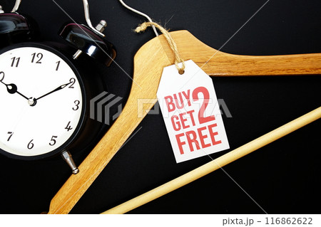 Buy 2 Get 2 Free on price tag with wooden clothes hanger and alarm clock top view on black background Buy 2 Get 2 Free on price tag with wooden clothes hanger and alarm clock top view on black background 116862622