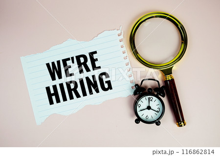 We're Hiring text on paper torn with alarm clock and magnifying glass top view on pink background We're Hiring text on paper torn with alarm clock and magnifying glass top view on pink background 116862814