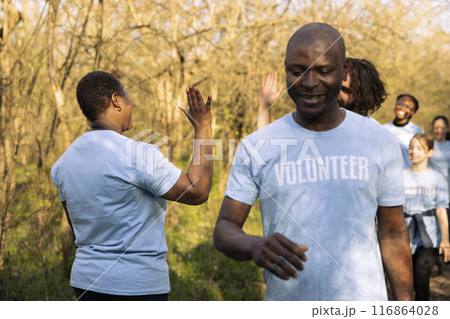 Team of volunteers sharing high five praising each other after a successful activity, finishing garbage and plastic cleanup. Proud joyful environmentalists enjoying their preservation mission. Team of volunteers sharing high five praising each other after a successful activity, finishing garbage and plastic cleanup. Proud joyful environmentalists enjoying their preservation mission. 116864028