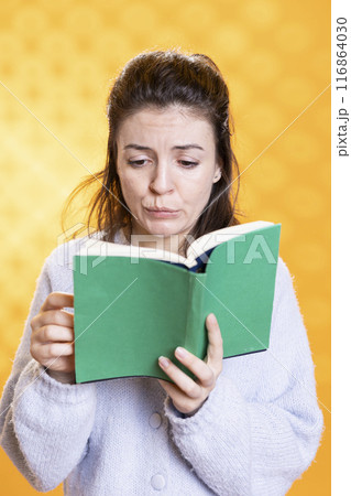 Woman with worried look on face biting lips from stress while gathering information for school exam in book, studio background. Student feeling tense before university assessment, reading textbook 116864030