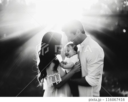 A loving family moment captured in black and white with sunlight streaming through, highlighting the joy and togetherness of parents and a child. 116867416