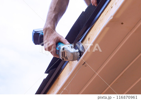 An employee cuts off vinyl soffit panels to given size on facade ceiling of new home 116870961