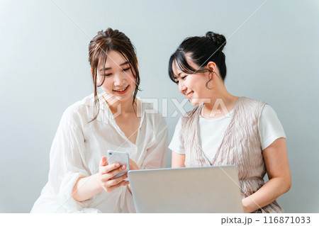 家で一緒にスマホとノートパソコンを使う女性・友達・ママ友・仲間 116871033